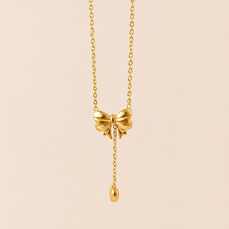 Gold tone necklace with a bow pendant on a beige background