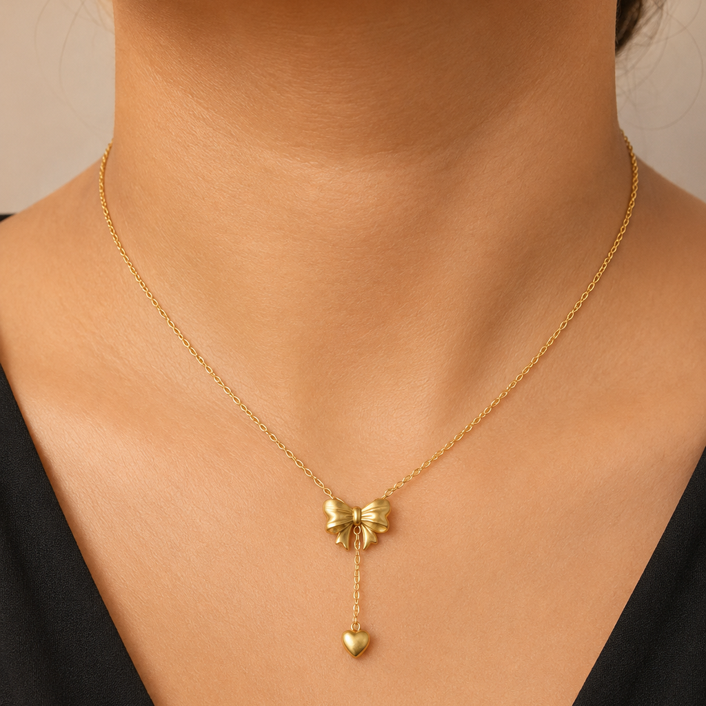 Gold tone necklace with a bow and heart pendant on a person wearing a black top.
