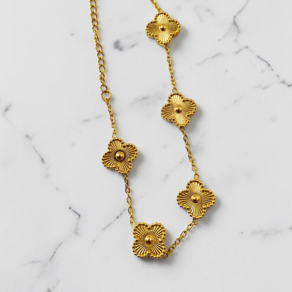 Gold tone necklace with floral designs on a marble background