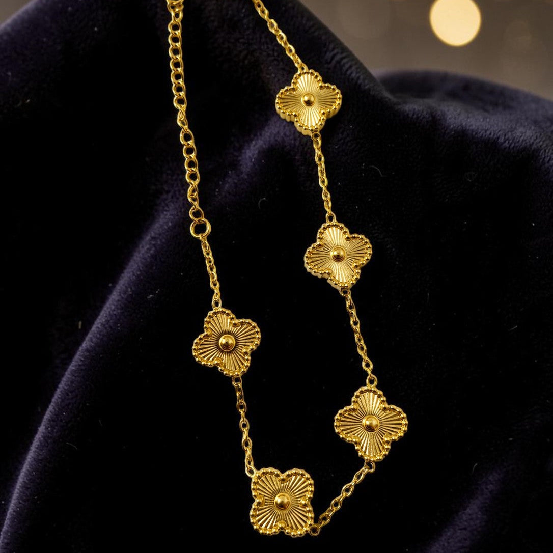 Gold tone floral chain necklace on a dark fabric background with blurred lights in the background