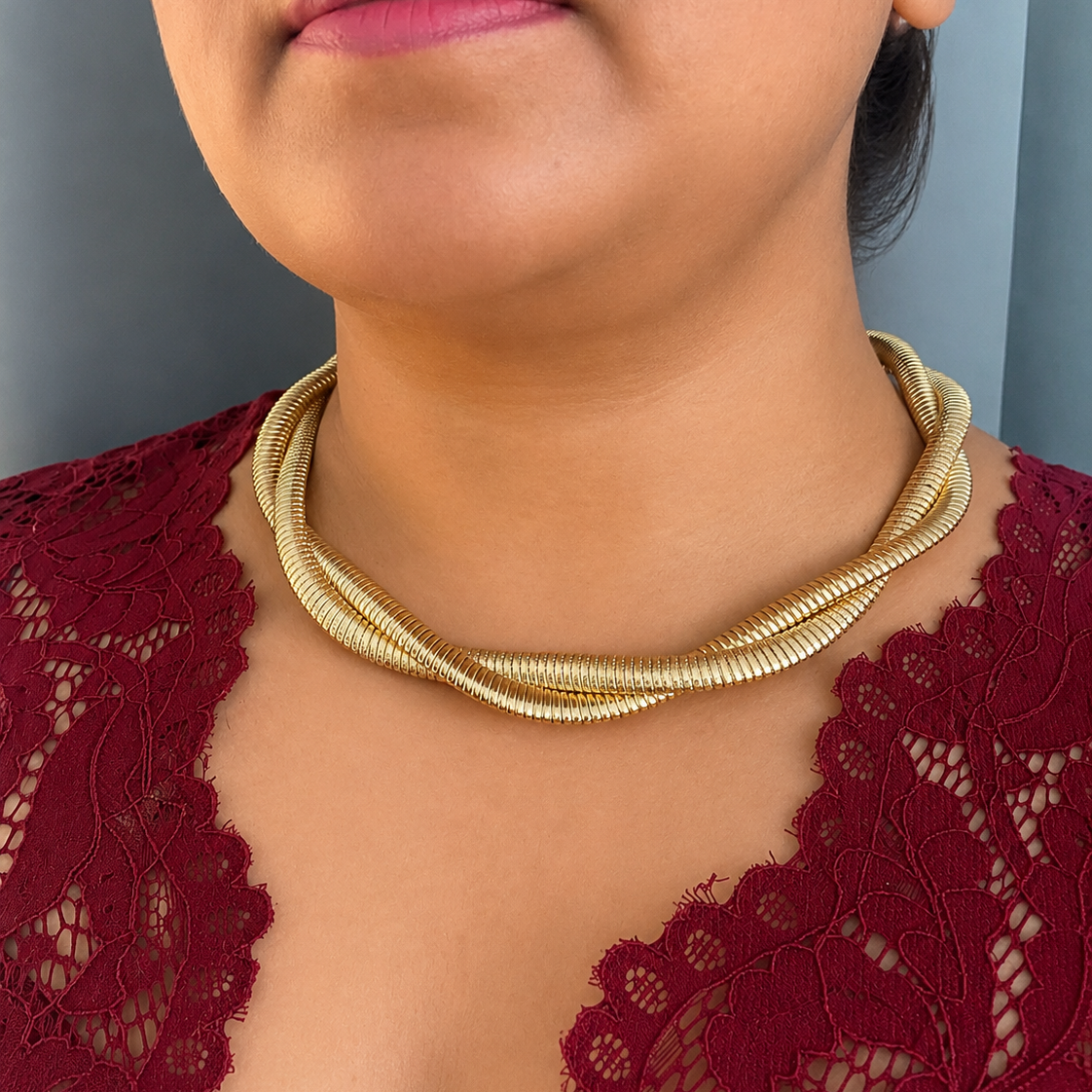 Close-up of a person wearing a gold necklace with a red lace top.