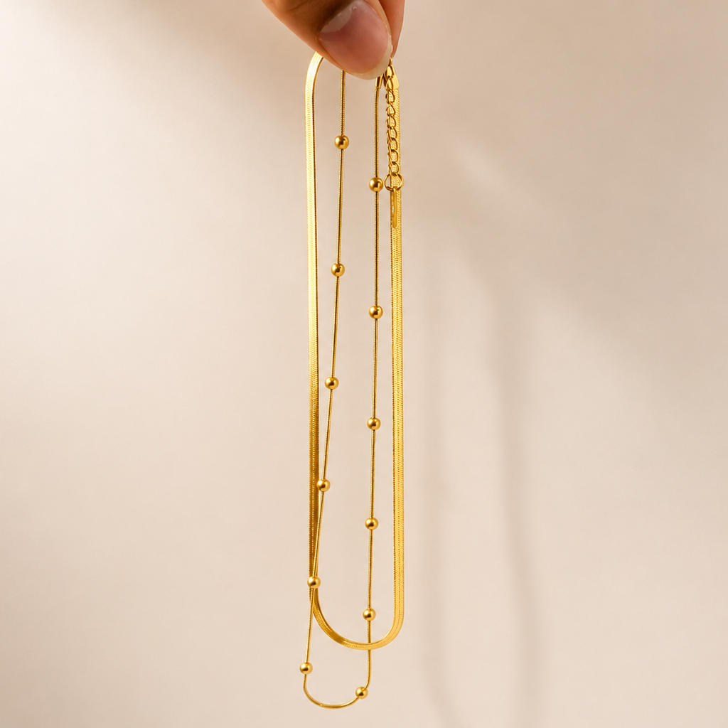 Gold tone necklace held by a hand against a beige background