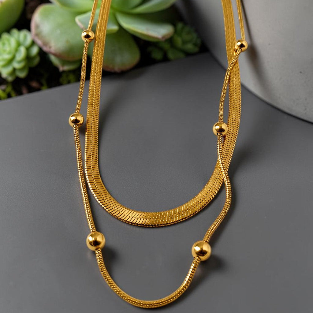 Gold tone necklace on a dark surface with succulents in the background