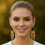 Woman wearing gold tone hoop earrings with fringe details against a blurred background