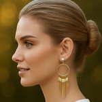 Woman wearing gold hoop earrings with fringe details against a blurred background