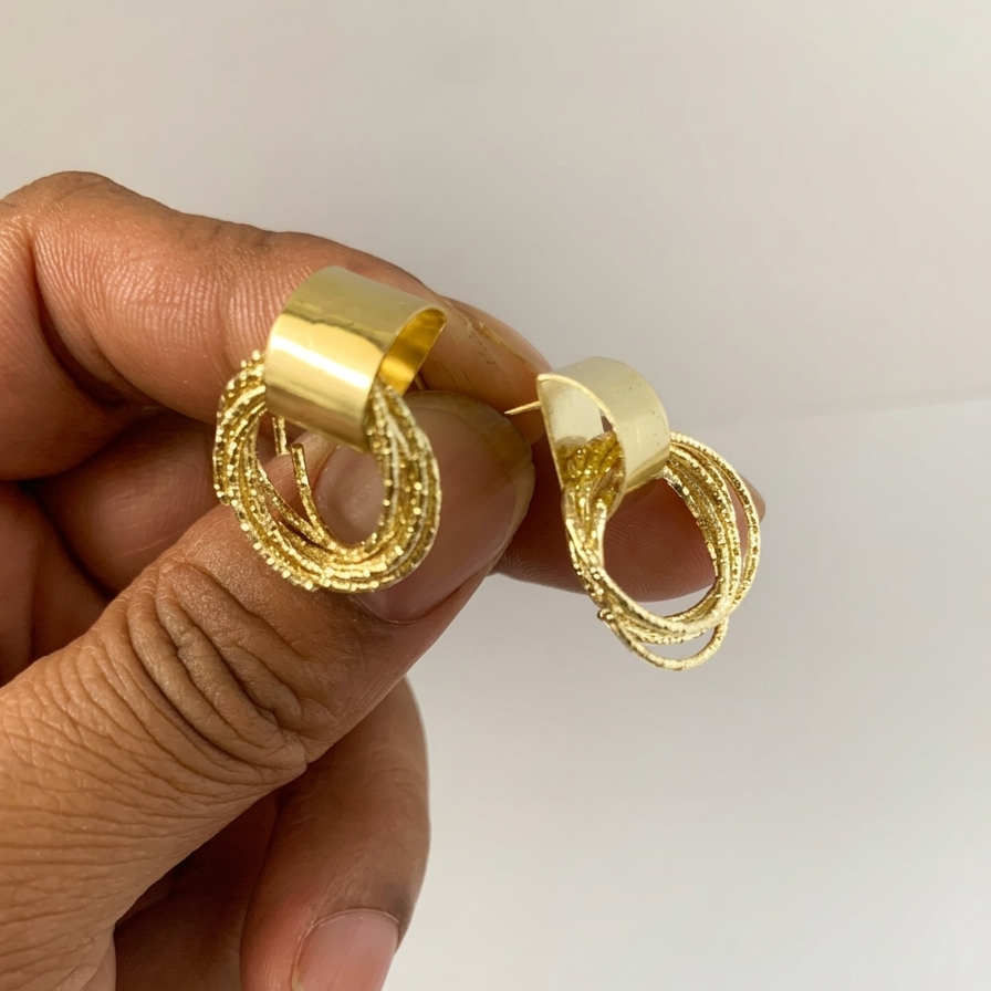 Gold hoop earrings held between fingers against a plain background
