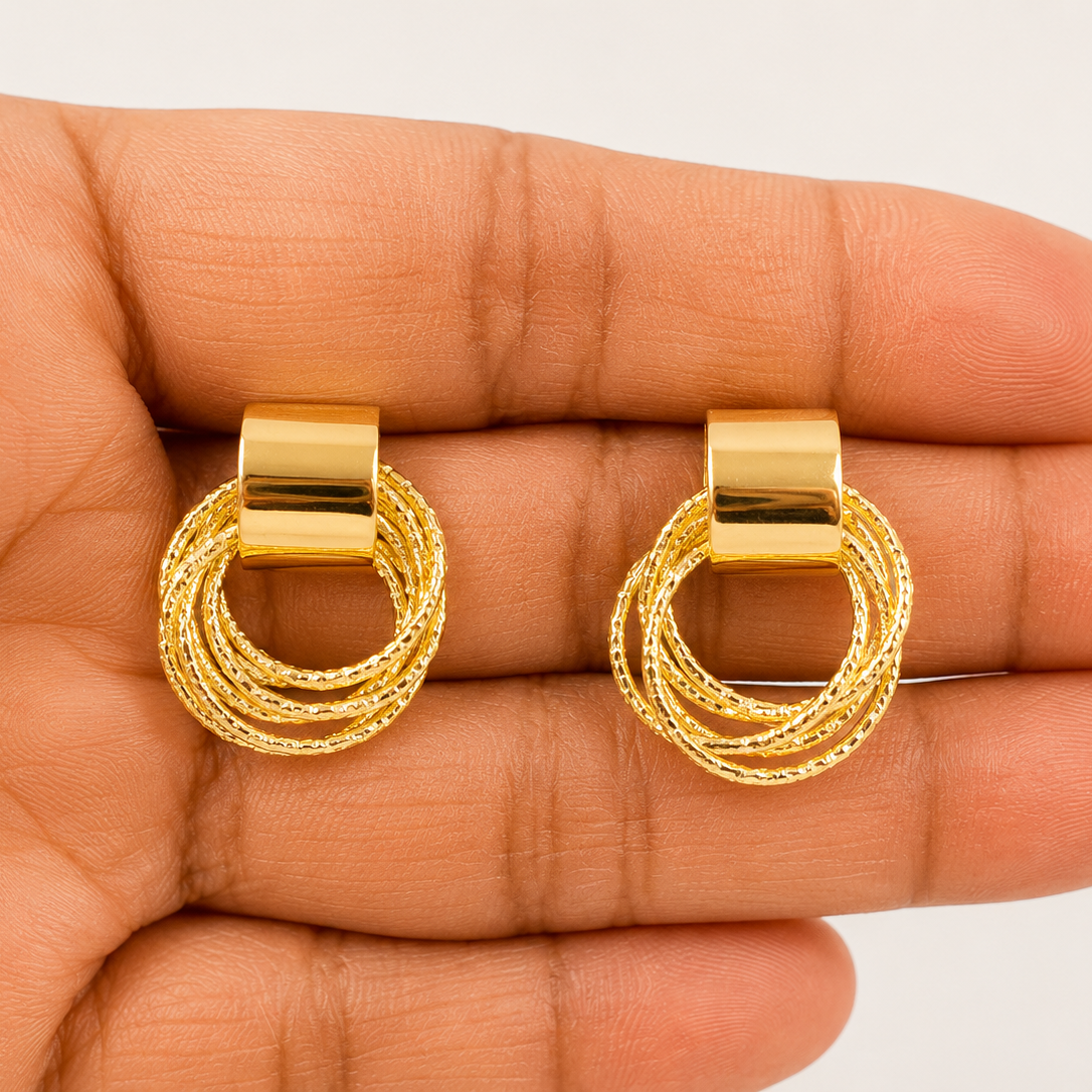 Gold tone hoop earrings held between fingers against a neutral background