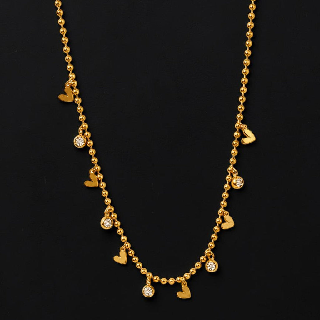 Gold tone necklace with heart and round pendants on a black background