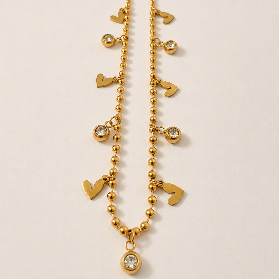 Gold tone necklace with heart and round charm on a beige background