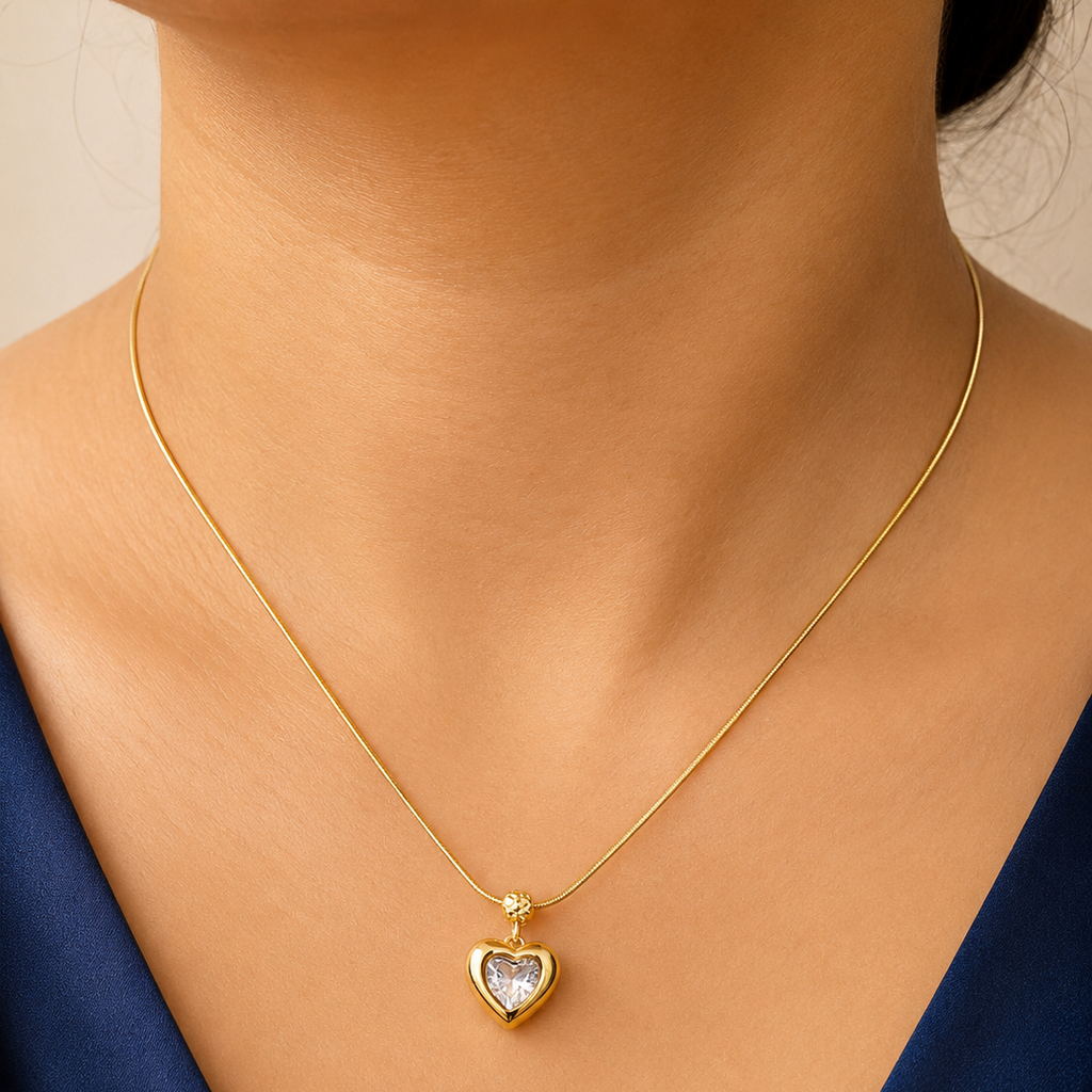 Gold tone necklace with a heart-shaped pendant on a person wearing a blue top.