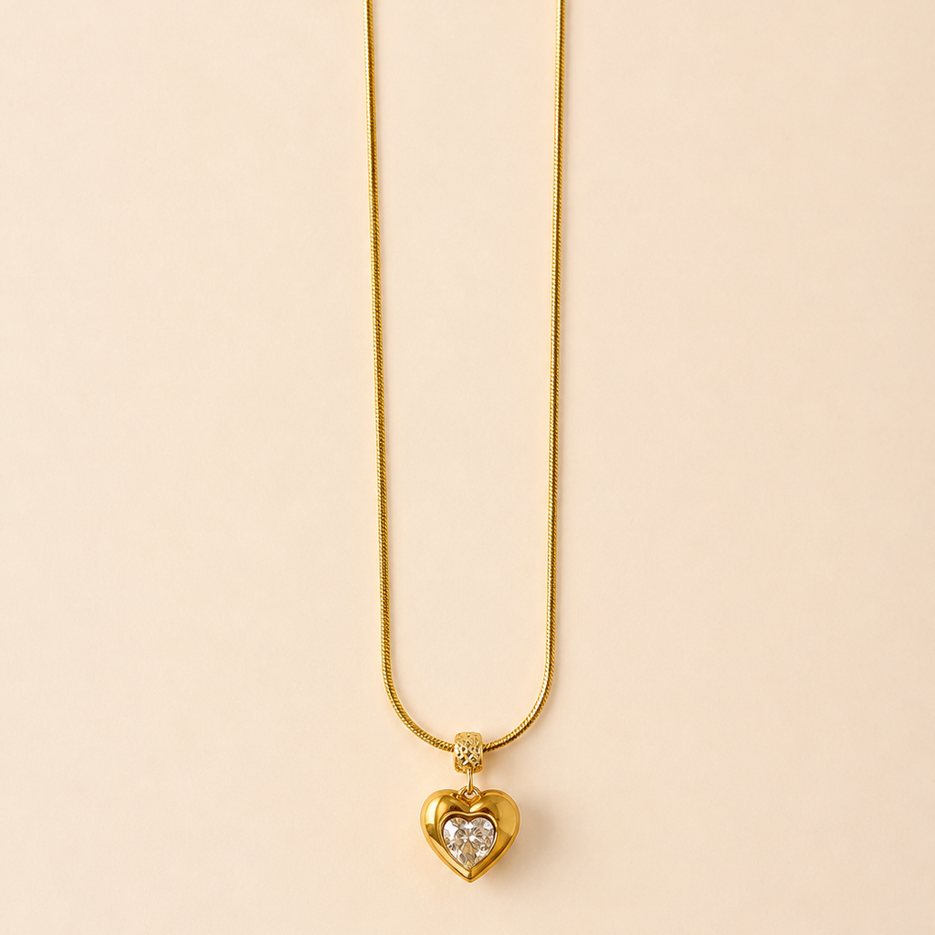 Gold tone necklace with a heart-shaped pendant on a beige background