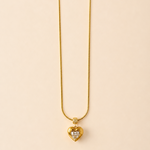 Gold tone necklace with a heart-shaped pendant on a beige background
