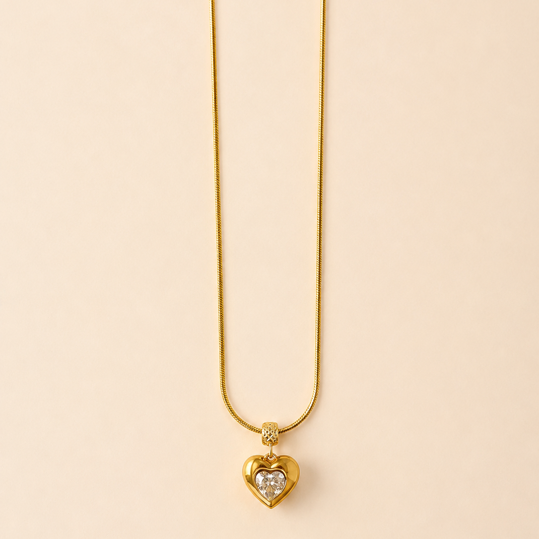 Gold tone necklace with a heart-shaped pendant on a beige background