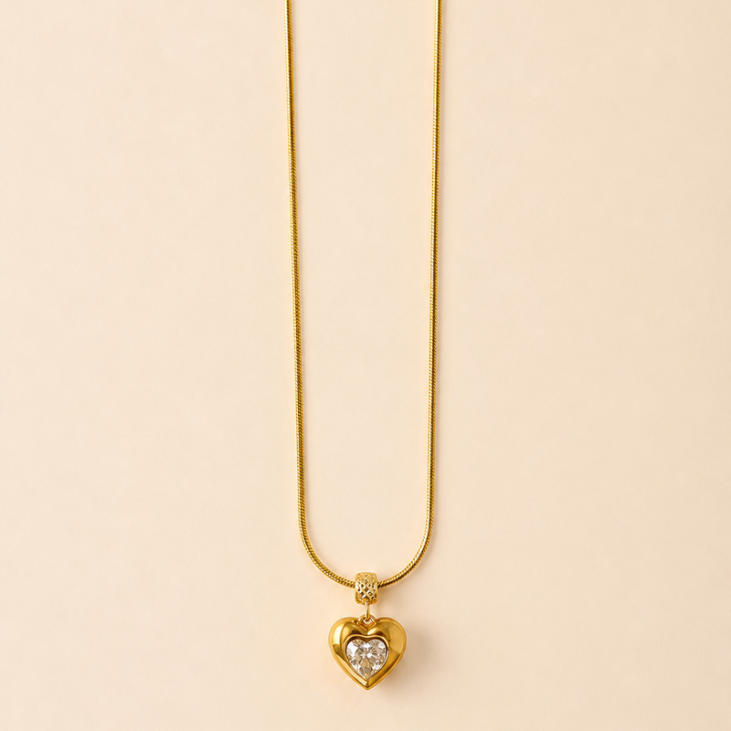 Gold tone necklace with a heart-shaped pendant on a beige background