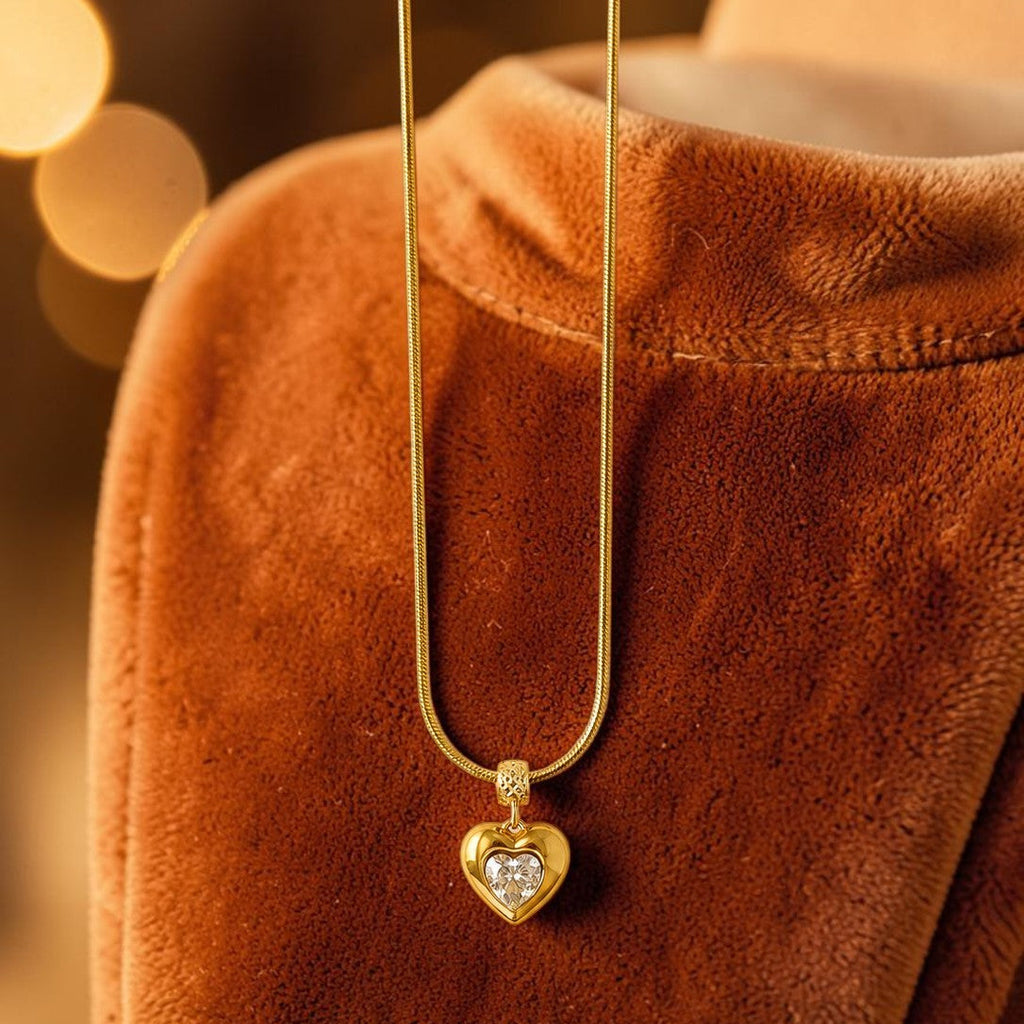 Gold tone necklace with a heart-shaped pendant on a brown textured surface with blurred lights in the background