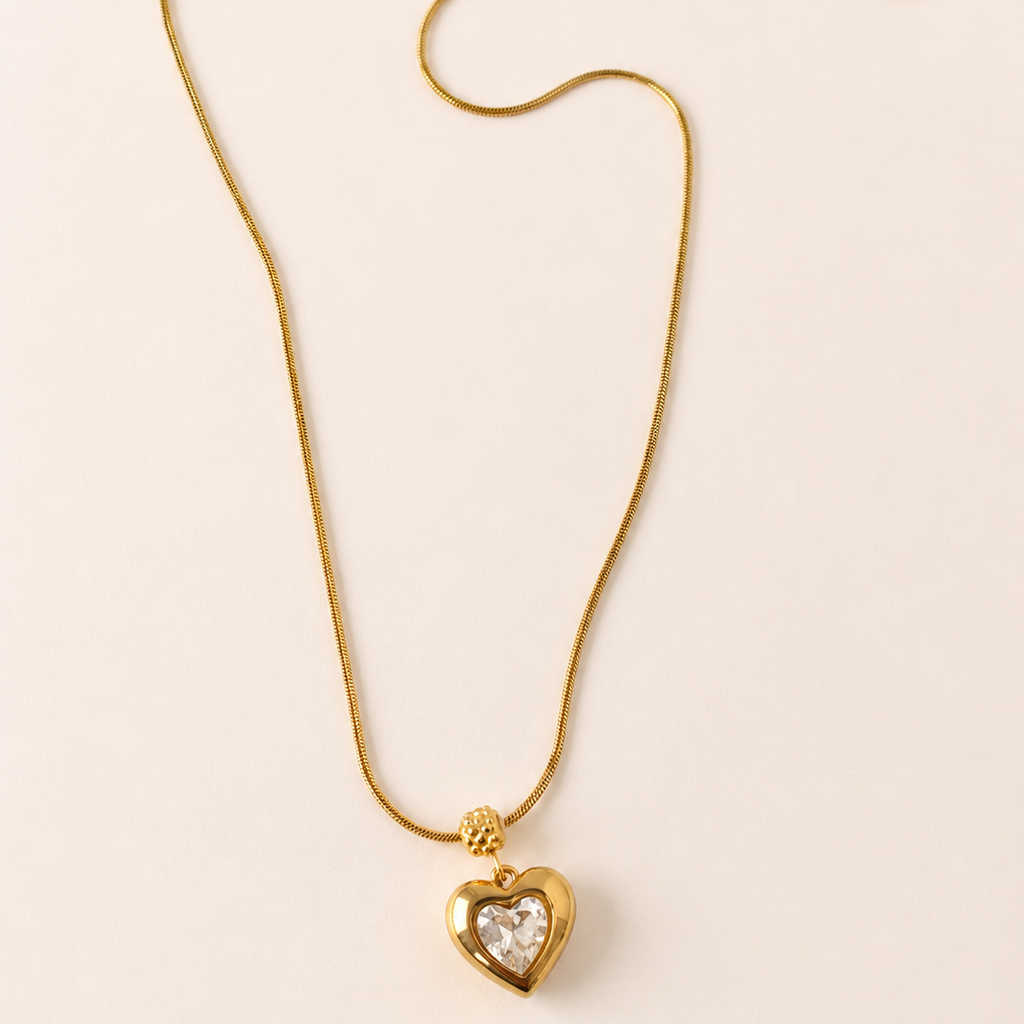 Gold tone necklace with a heart-shaped pendant on a light beige background