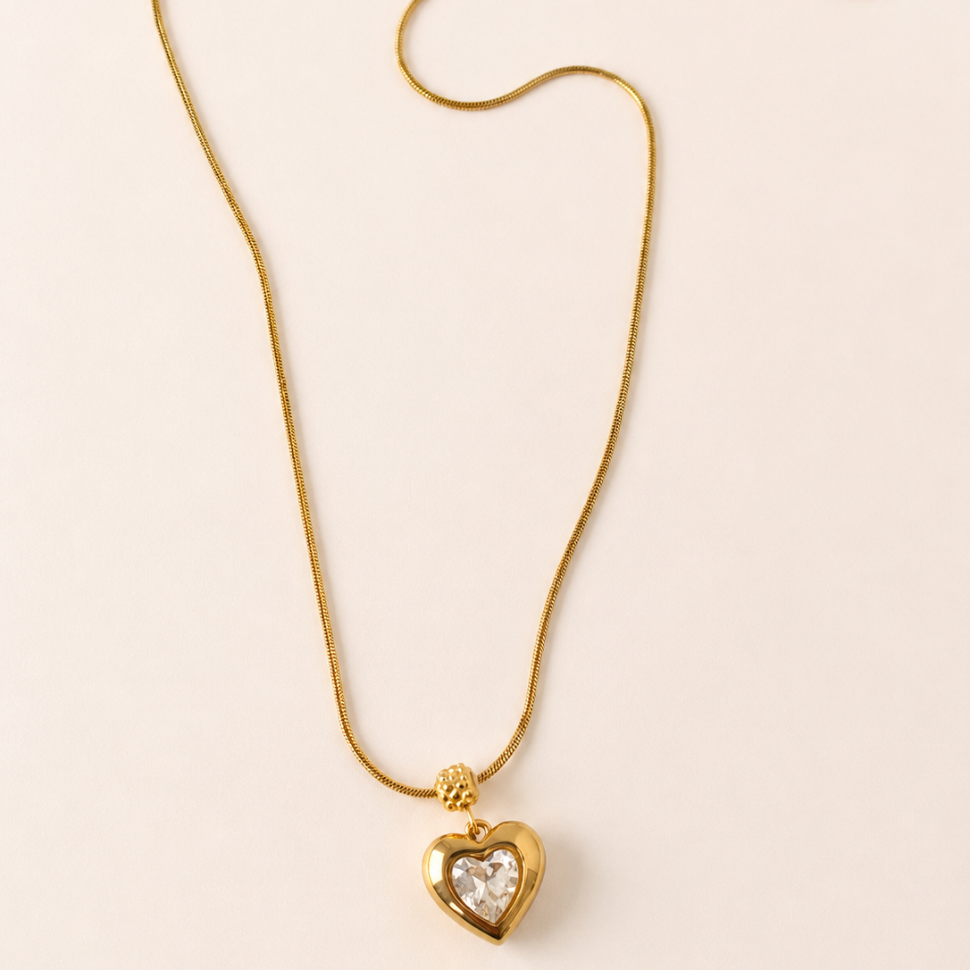Gold tone necklace with a heart-shaped pendant on a light beige background