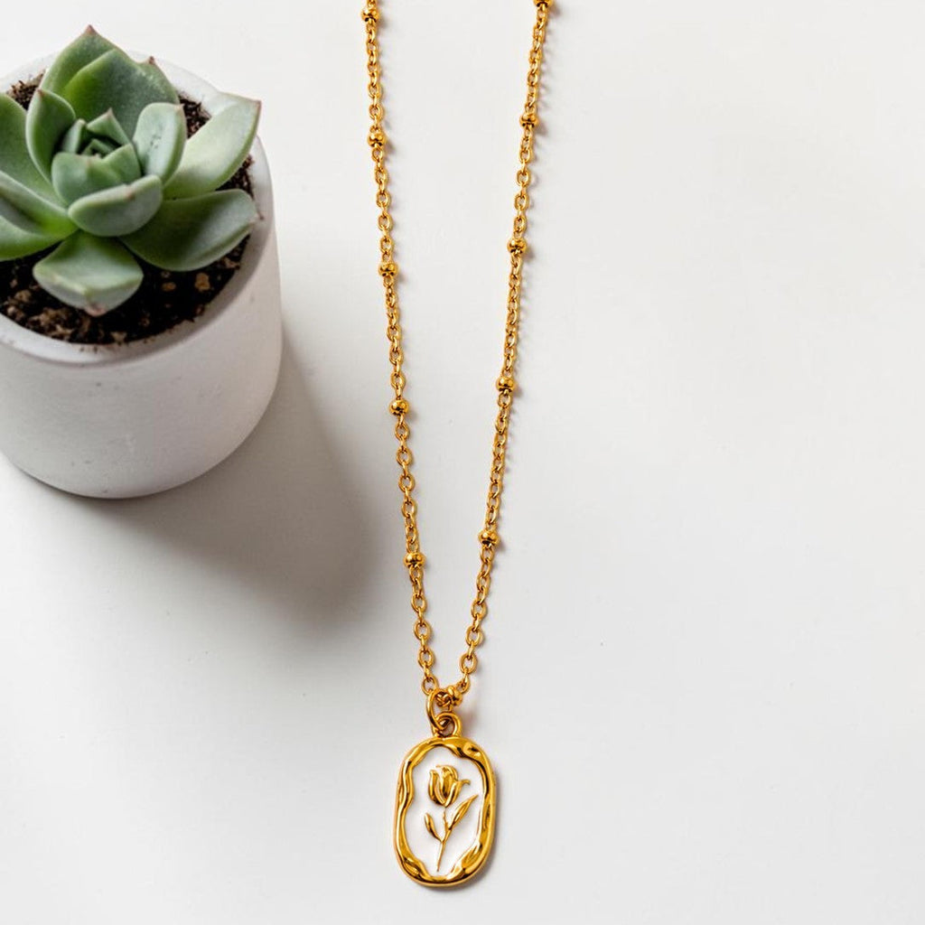 Gold tone necklace with a pendant next to a small potted succulent on a white surface