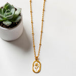 Gold tone necklace with a pendant next to a small potted succulent on a white surface