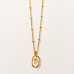 Gold tone necklace with a pendant on a light beige background