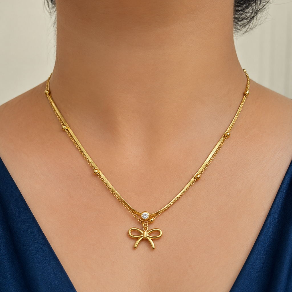 Gold tone necklace with a bow pendant on a person wearing a blue top.