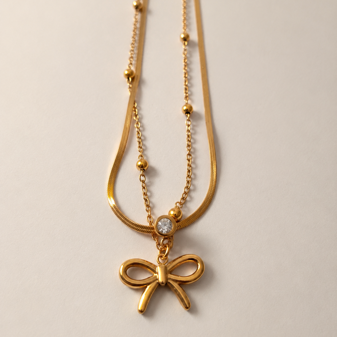 Gold tone necklace with a bow pendant on a light gray background