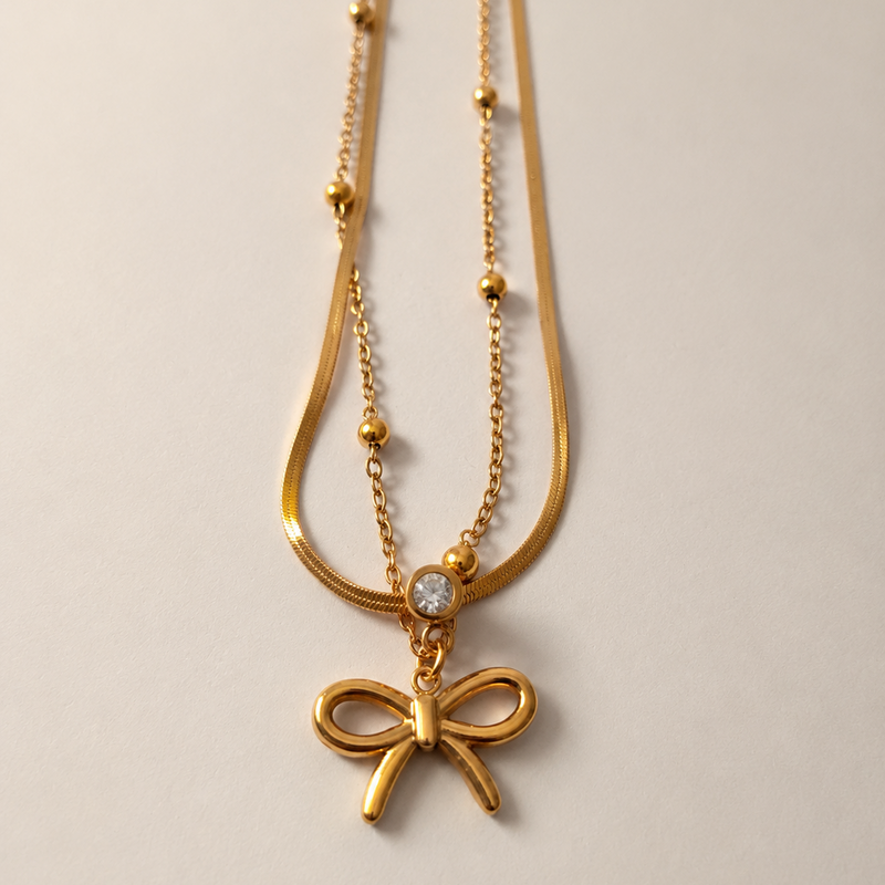 Gold tone necklace with a bow pendant on a light gray background