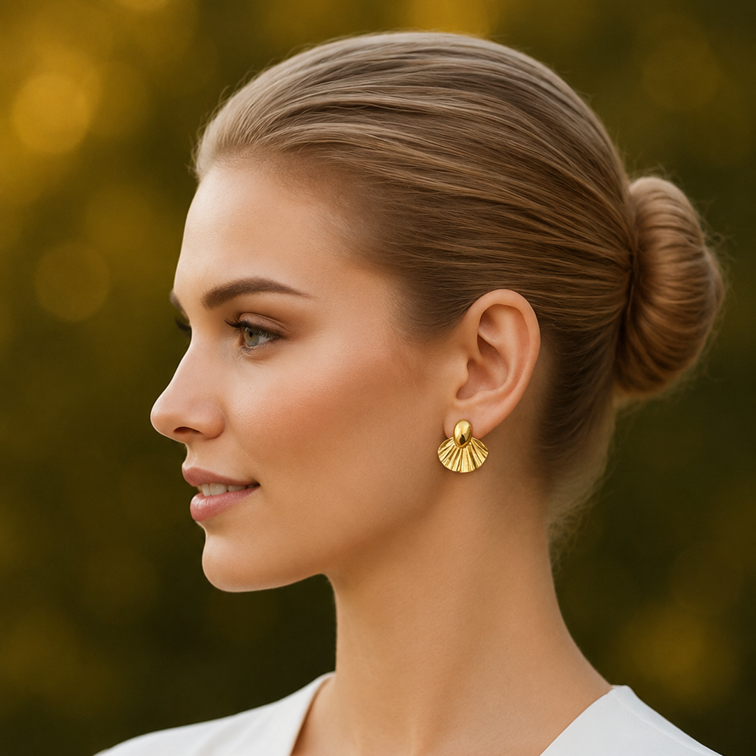 Woman with styled hair and gold tone earrings against a blurred natural background