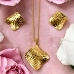 Gold tone necklace and earrings on a pink surface with pink and white roses.e 
