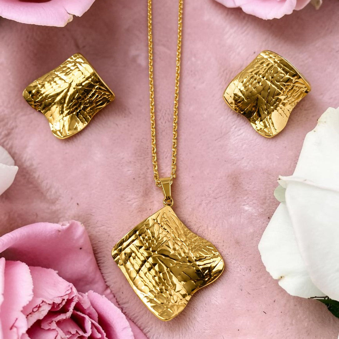 Gold tone necklace and earrings on a pink surface with pink and white roses.e 