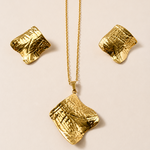 Golden necklace with textured pendant and matching earrings on a beige background