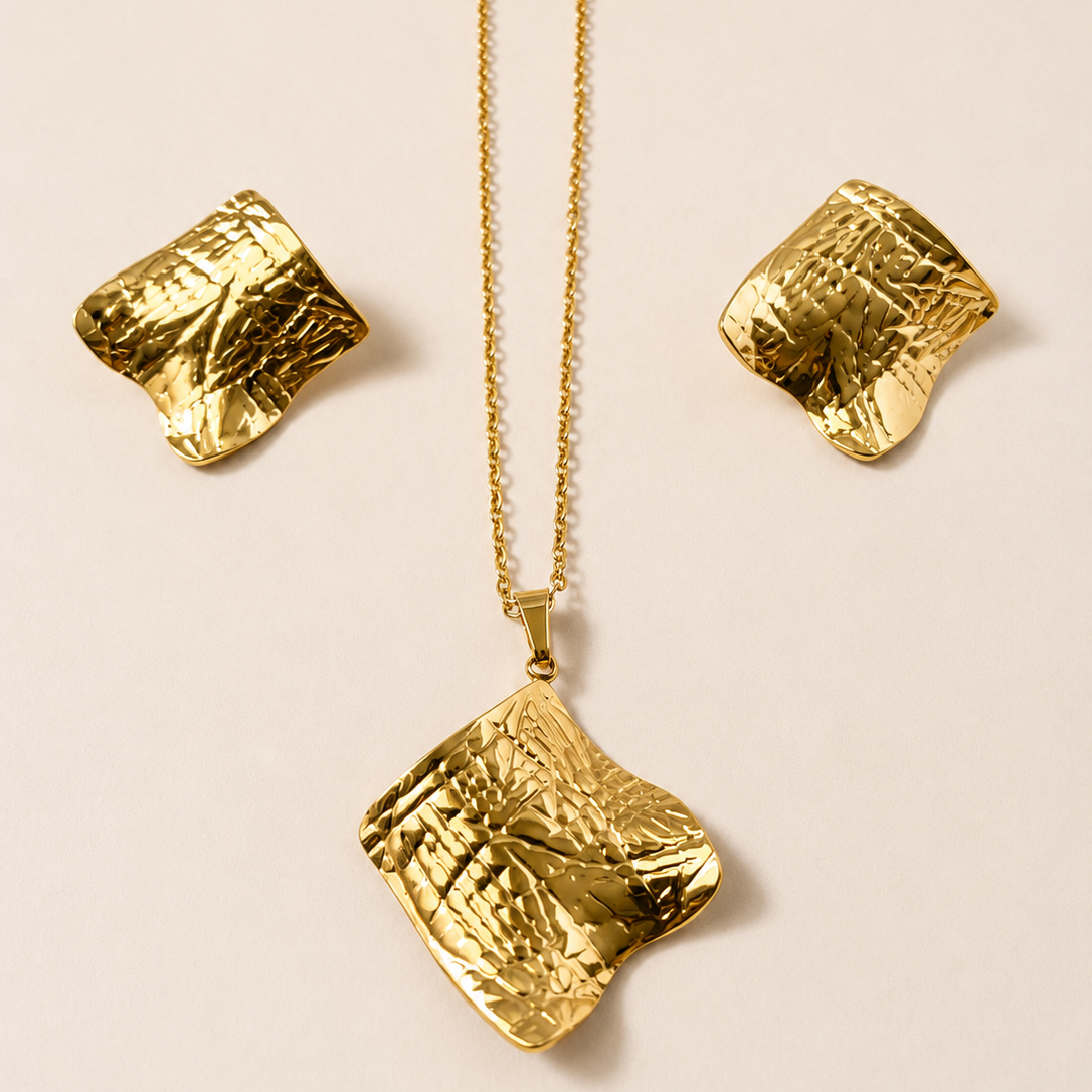 Golden necklace with textured pendant and matching earrings on a beige background