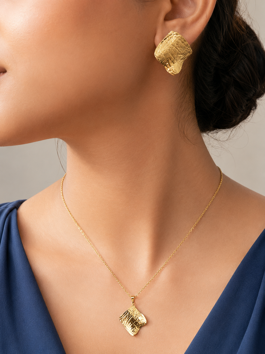 Gold tone earrings and necklace on a person with a neutral background