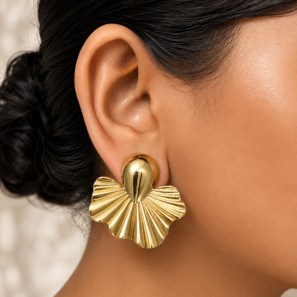 Golden shell-shaped earrings worn by a person with a neutral background