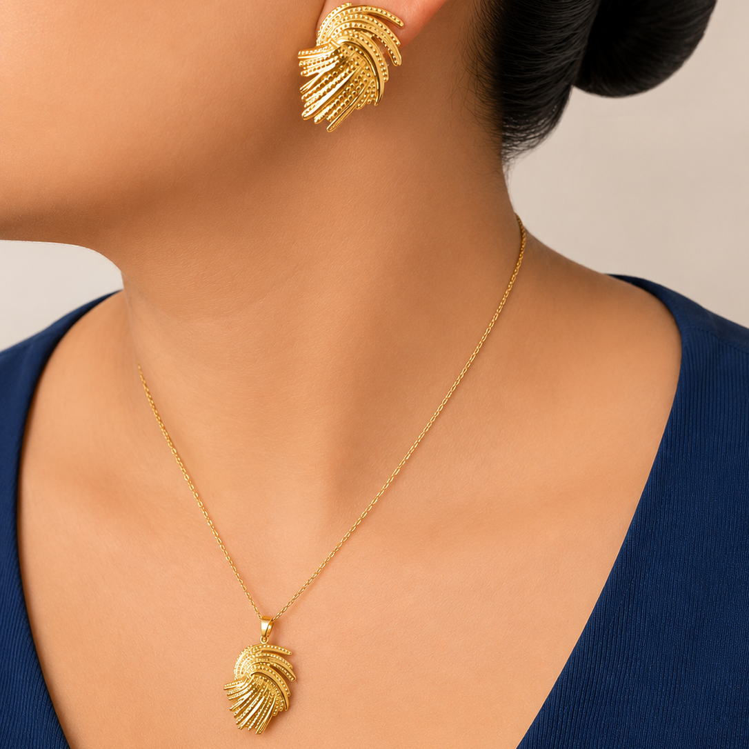 Gold tone earrings and necklace on a person against a neutral background