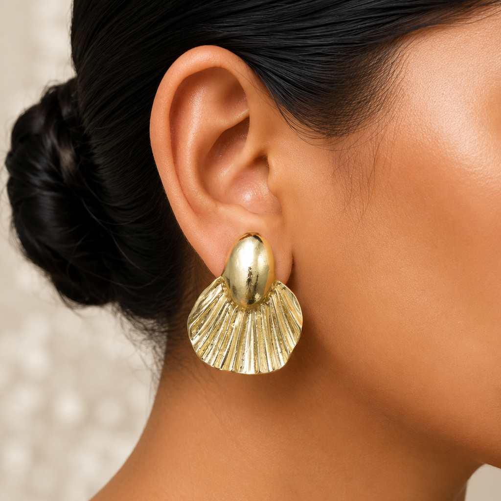 Close-up of a person wearing a golden shell-shaped earring with a neutral background