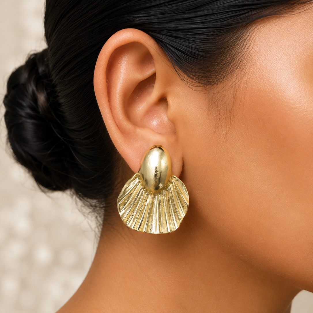 Close-up of a person wearing a golden shell-shaped earring with a neutral background