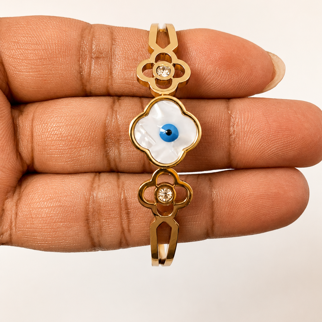 Golden pendant with an eye design held between fingers on a beige background