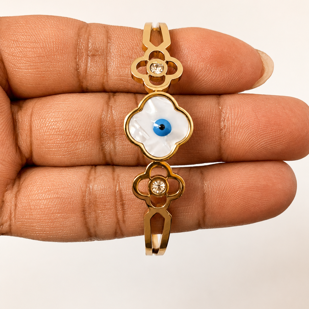 Golden pendant with an eye design held between fingers on a beige background
