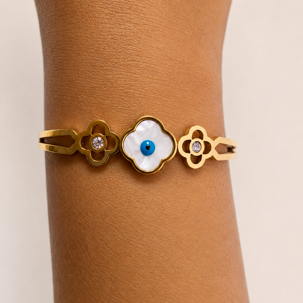 Golden bracelet with a central white stone and blue center worn on a wrist against a beige background