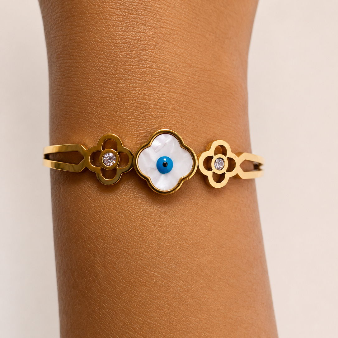 Golden bracelet with a central white stone and blue center worn on a wrist against a beige background