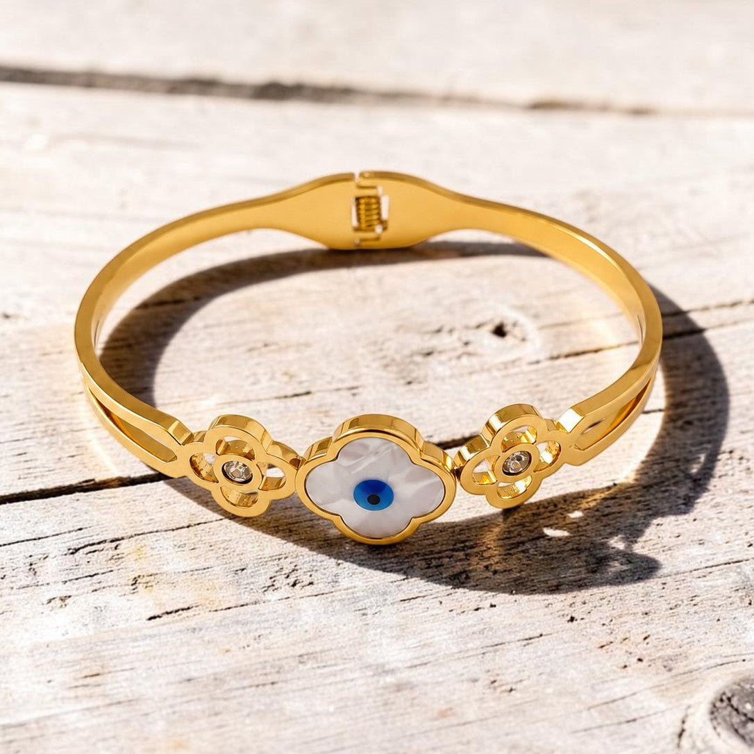 Golden bracelet with a blue eye design on a wooden surface