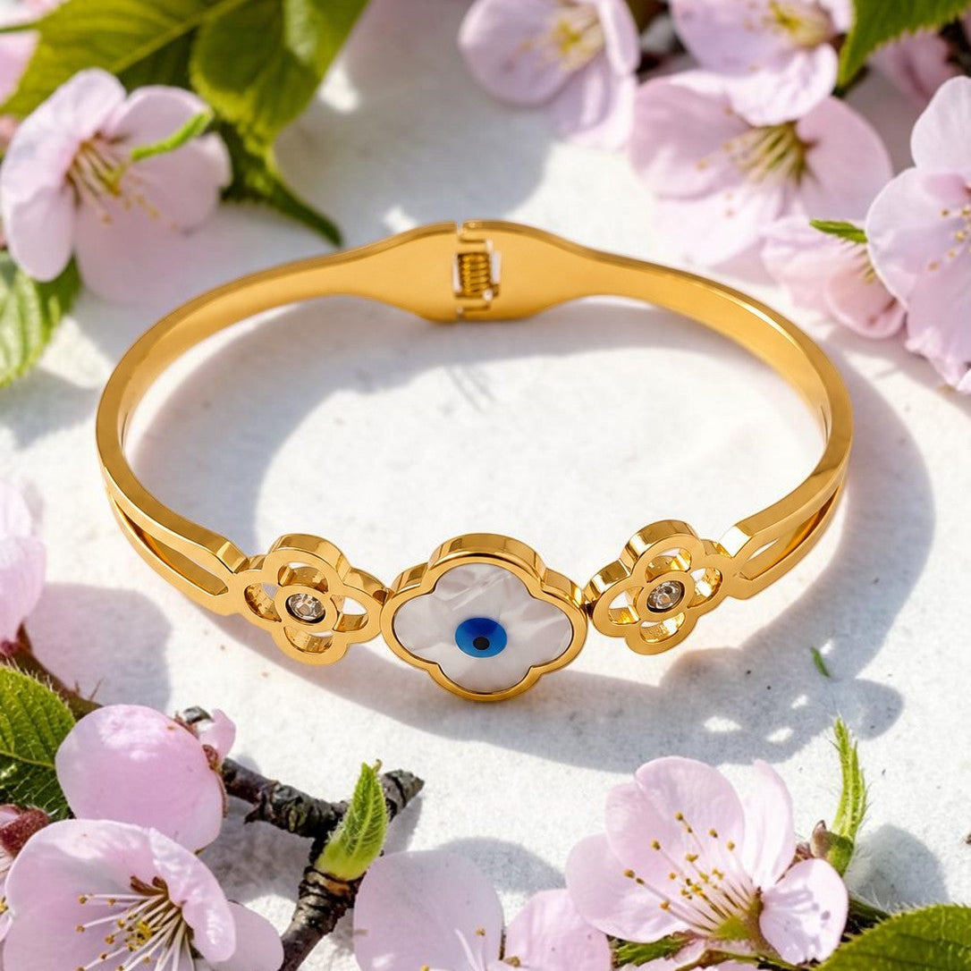 Golden bracelet with a blue gemstone on a white surface with pink flowers