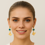 Woman wearing gold tone earrings with blue gemstones on a plain background