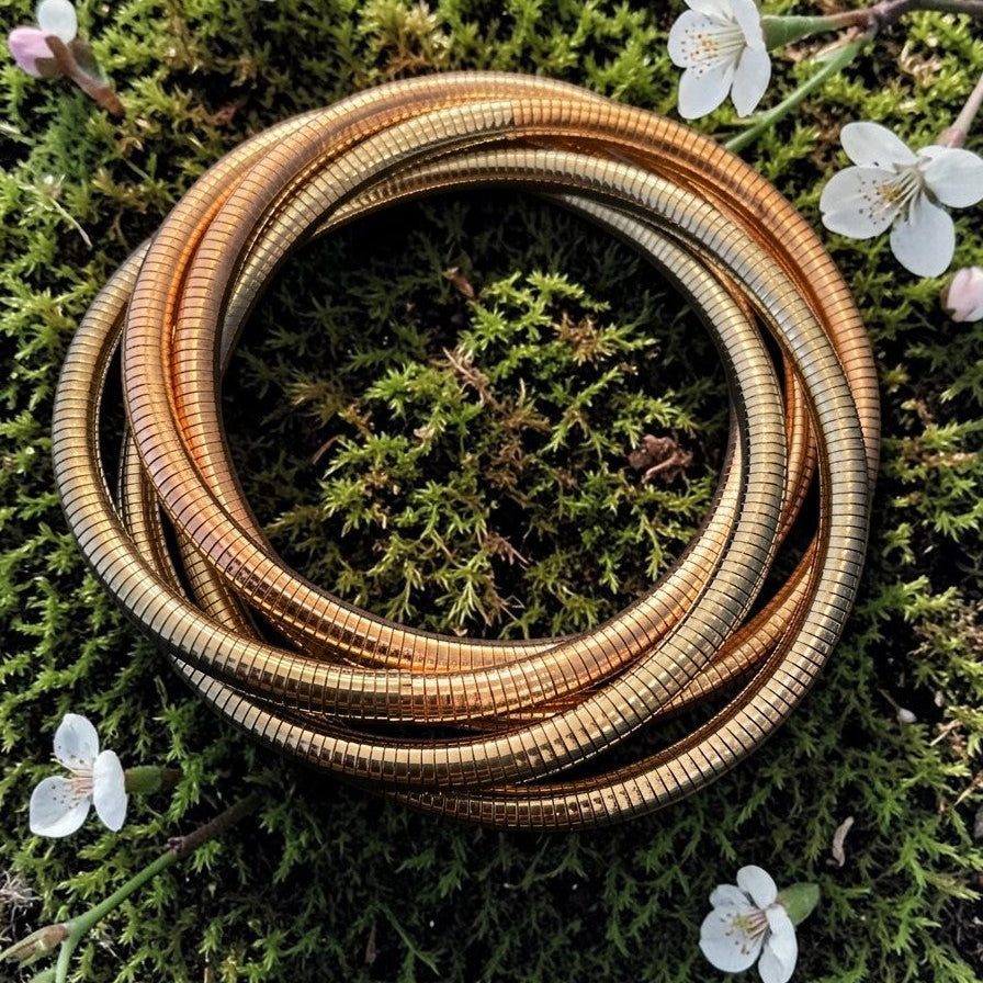 Coiled brass or bronze tube on a green mossy background with small white flowers