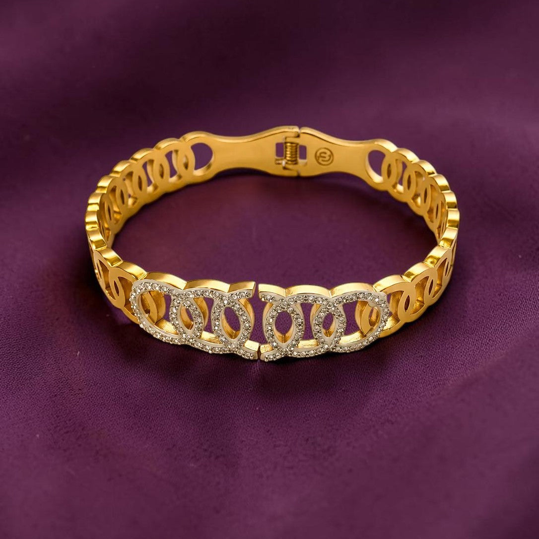 A gold link bracelet with a central row of clear pavé-set stones, displayed on a dark purple satin fabric background.
