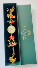 A gold-plated traditional Indian watch bracelet with red and white enamel details, presented inside an open dark green gift box next to its lid, which features the brand name 'SHINE & RISE'.