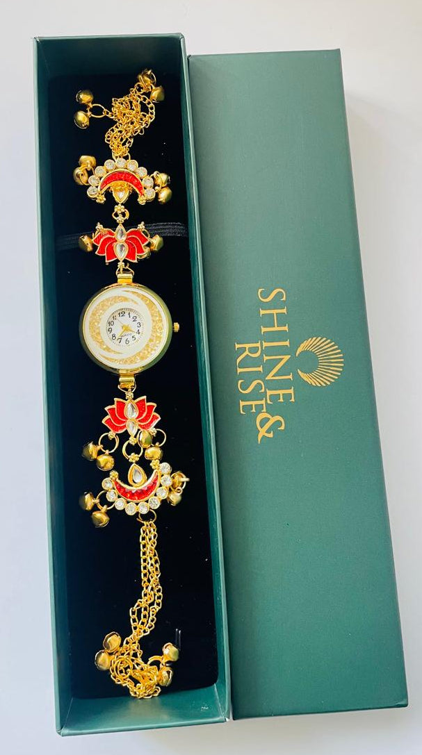 A gold-plated traditional Indian watch bracelet with red and white enamel details, presented inside an open dark green gift box next to its lid, which features the brand name 'SHINE & RISE'.