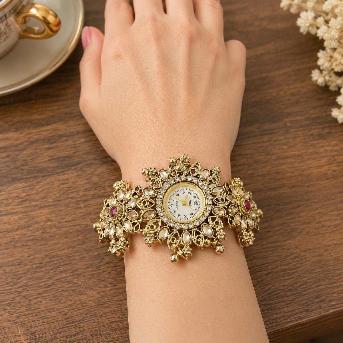 An ornate gold-toned watch with a wide, decorative bracelet-style band and a round dial, shown worn on a person's wrist over a wooden table.