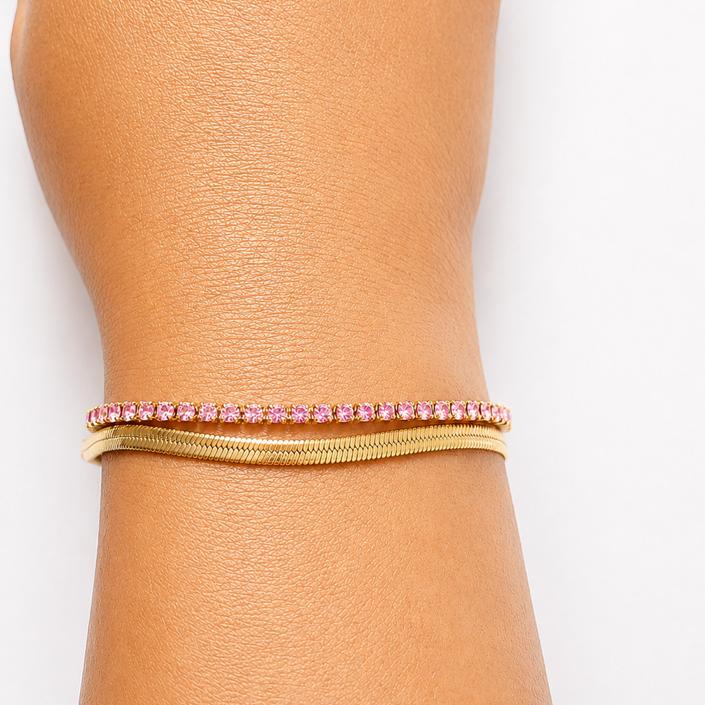 Gold tone bracelet with pink stones on a wrist against a white background